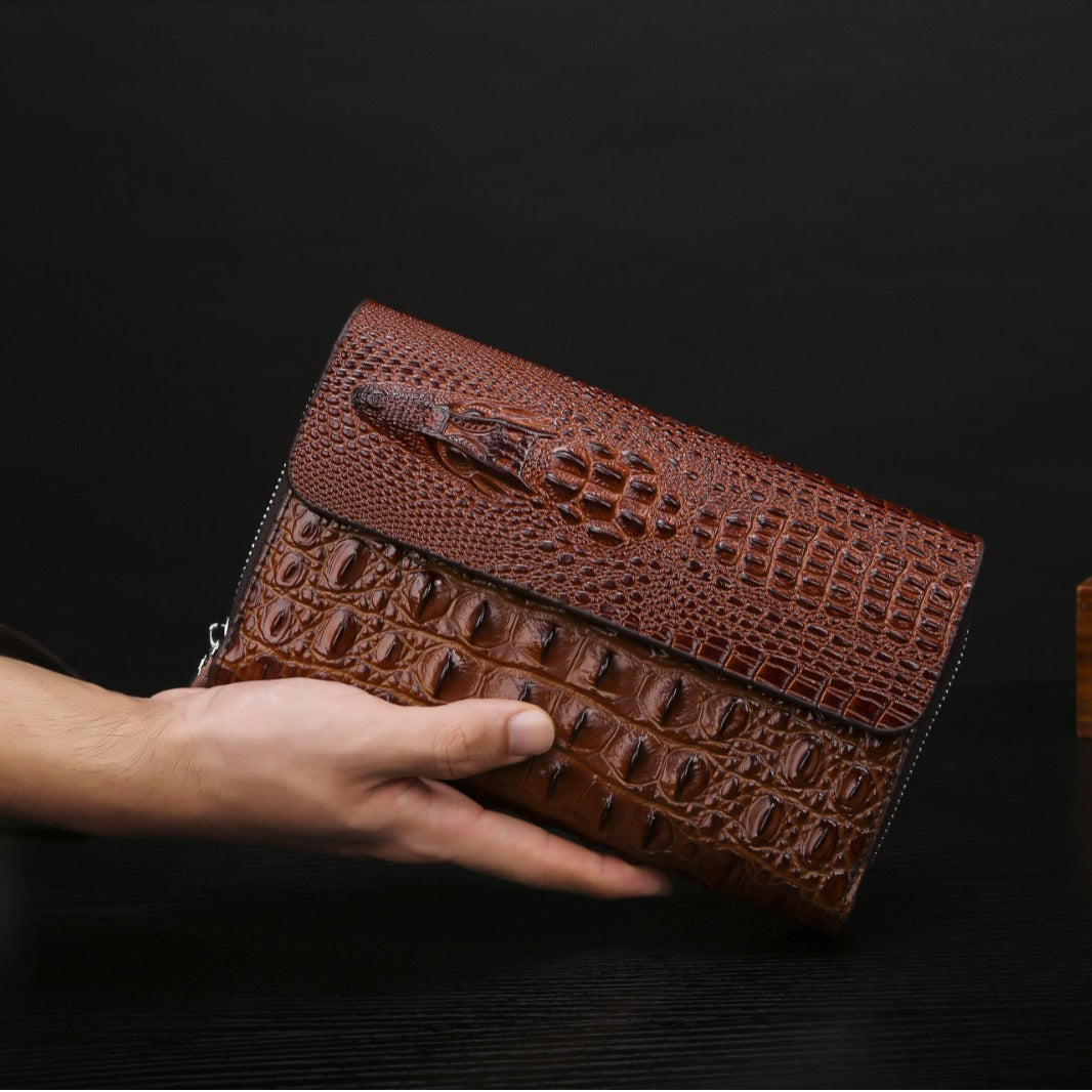 Brown crocodile-patterned clutch held by a hand against a dark background