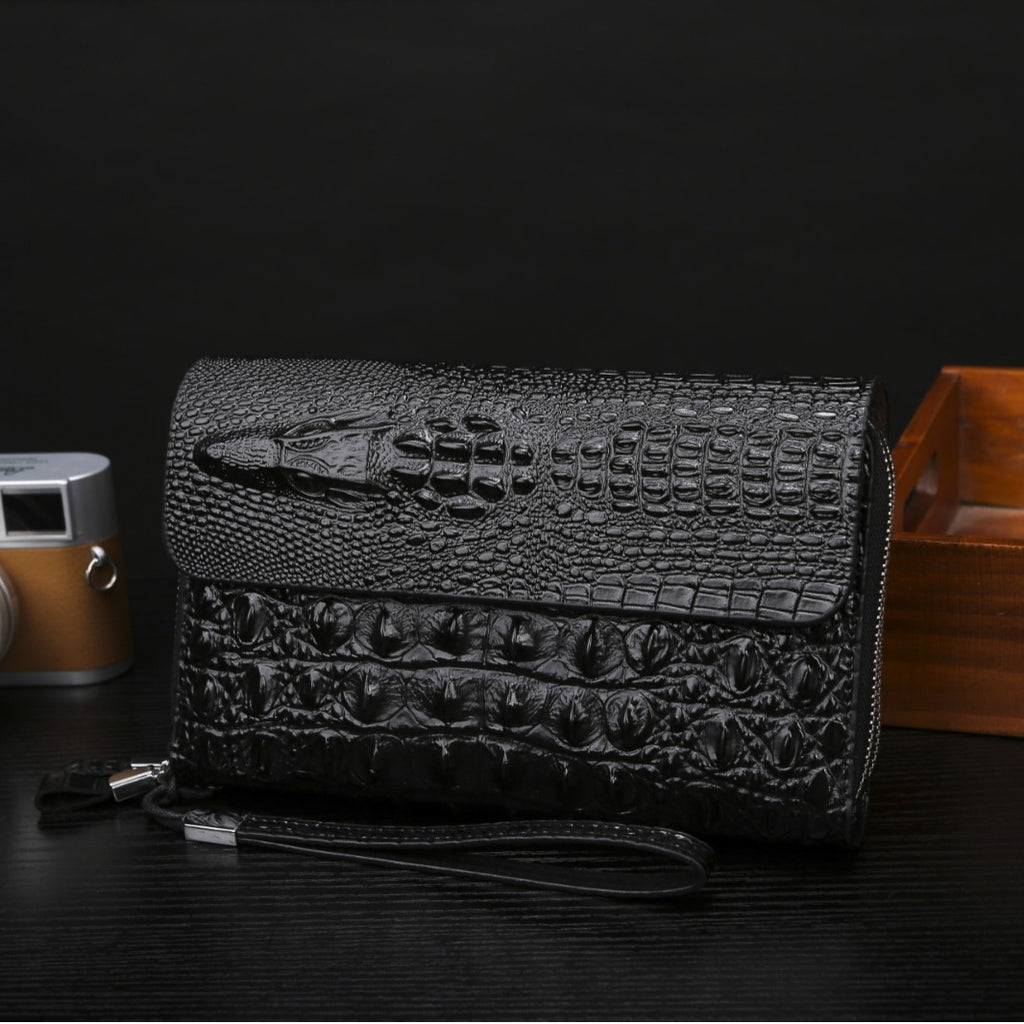 Black textured clutch bag on a dark surface with a camera and wooden box in the background