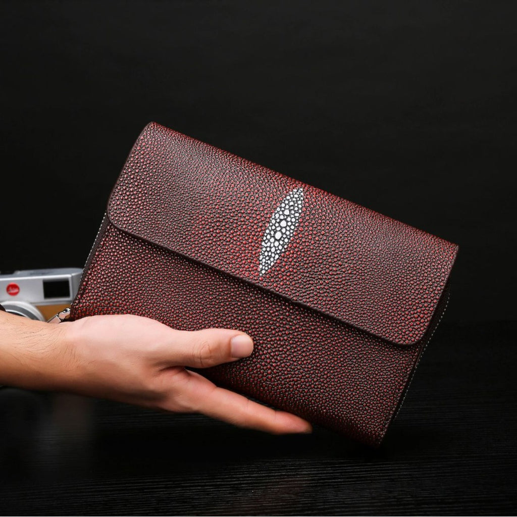 Brown leather clutch held by a hand against a dark background