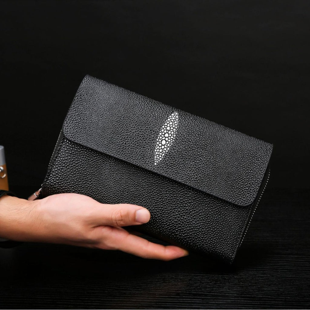 Black clutch bag with a decorative silver leaf held by a hand against a dark background