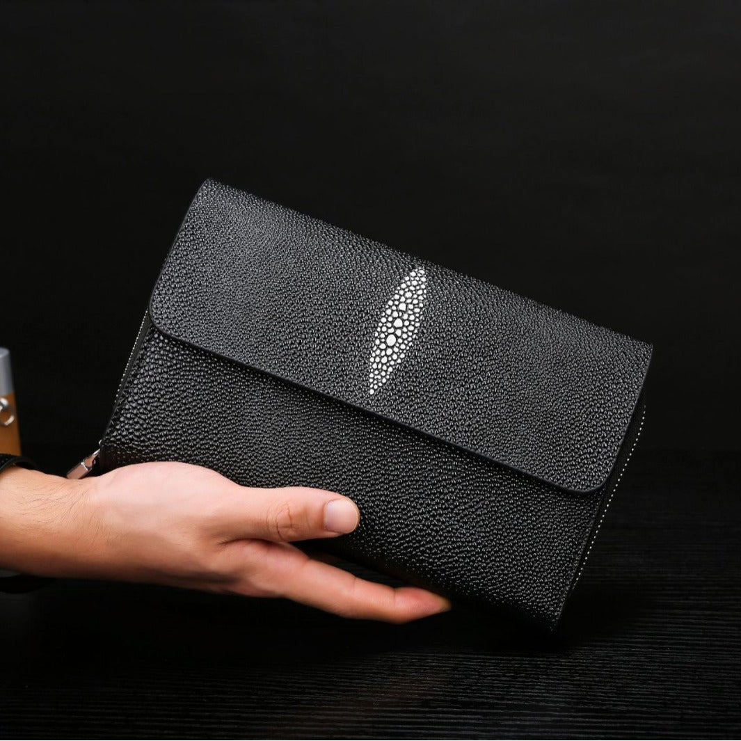 Black clutch bag with a decorative silver leaf held by a hand against a dark background